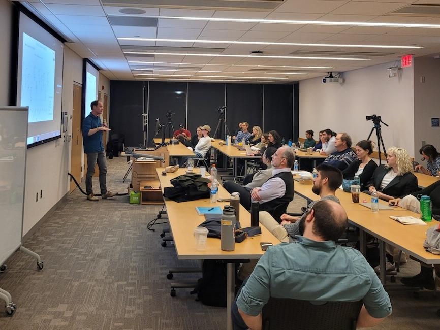  2024 Consortium on Moral Decision-Making Conference image shows a presenter leading a talk in a small room full of people seated at tables.