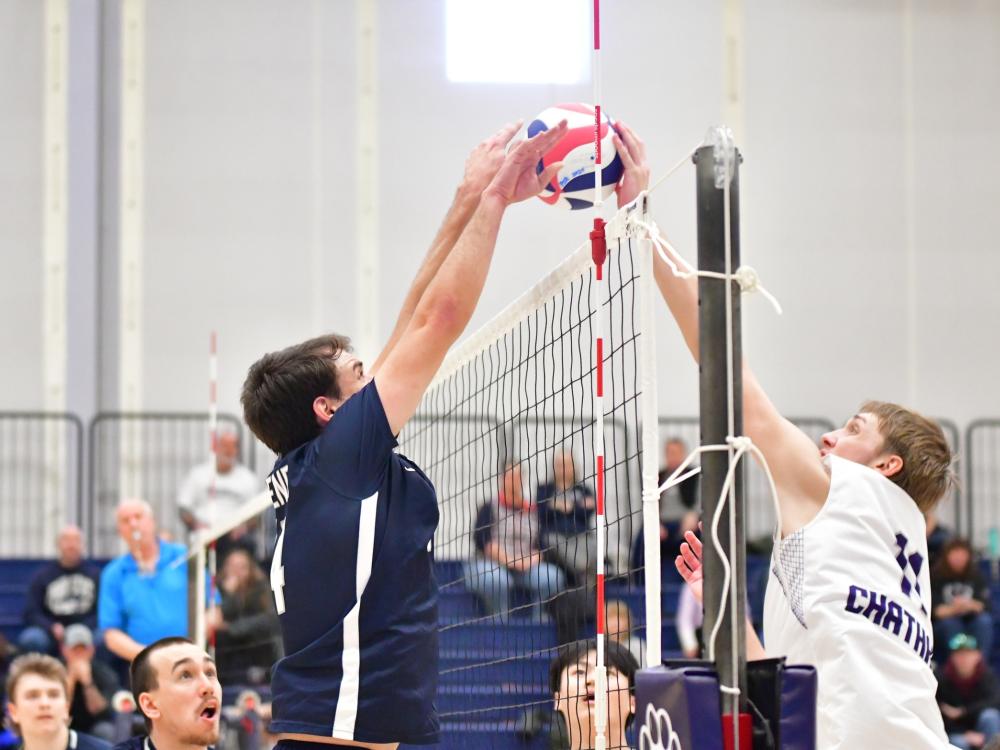 Two male volleyball players jump while facing each other at the net.