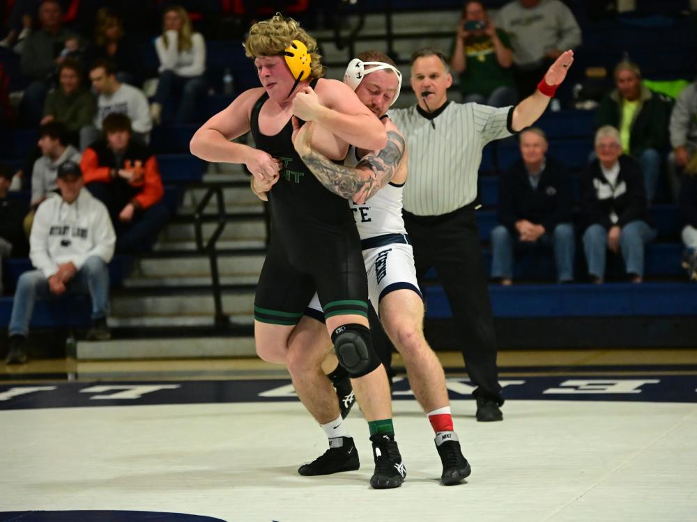 A Penn State Behrend wrestler grabs an opponent from  behind while standing.