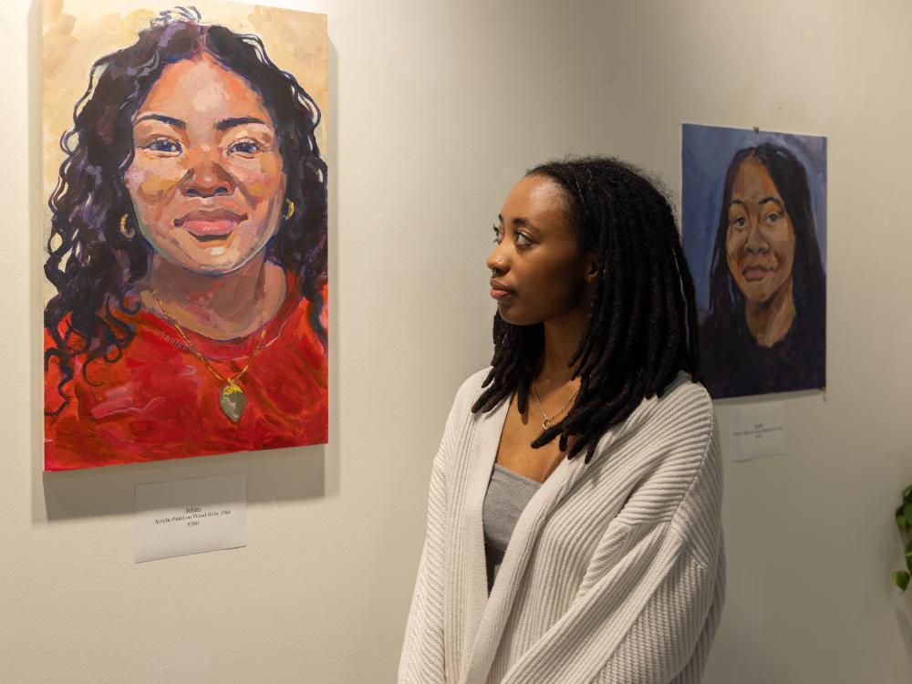 A young Black woman looks at a portrait on the wall.