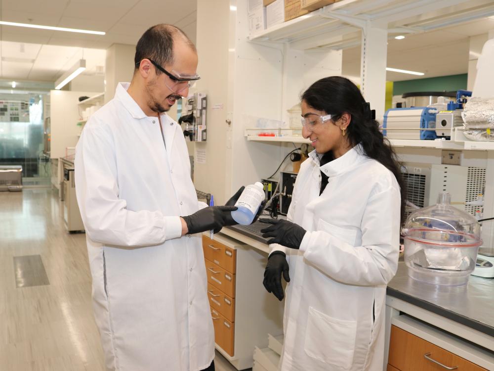 Two people in lab coats check a bottle of chemicals