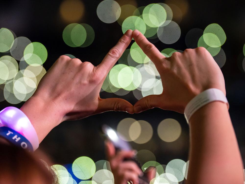 two hands in the air coming together to make a diamonds shape infront of bright lights