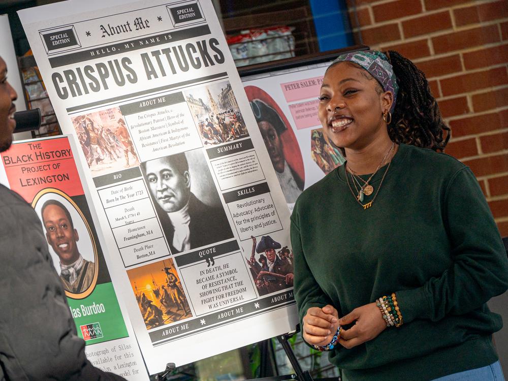 Students stand next to research posters and talk
