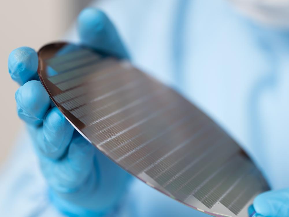 Two gloved hands holding a semiconductor wafer