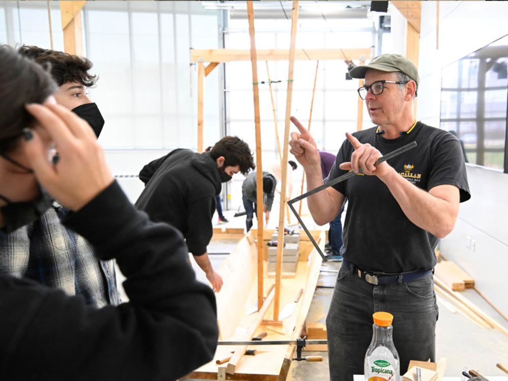 Students listening to man teach about building wooden boats