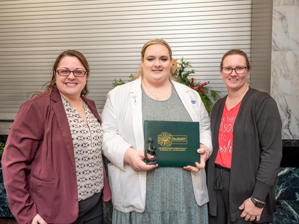 Three people stand in a row, one is holding an award certificate.