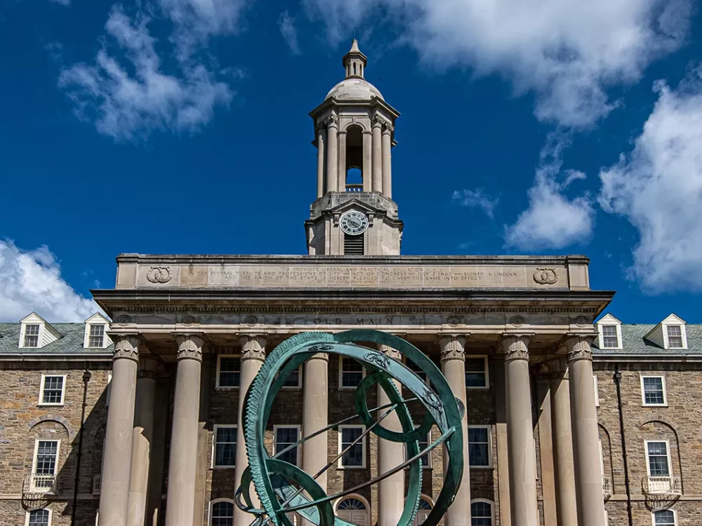 Old Main against a brilliant blue sky with the armilliary sphere in front