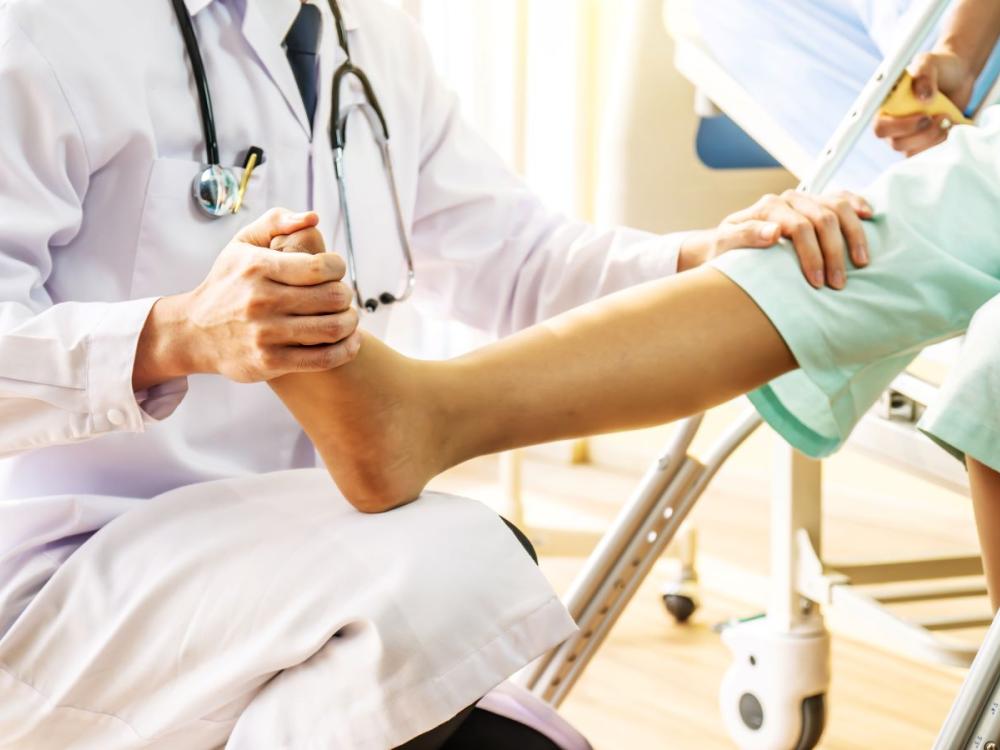 A physician, wearing a medical coat and stethoscope, is seated and holding onto a patient’s lower leg.