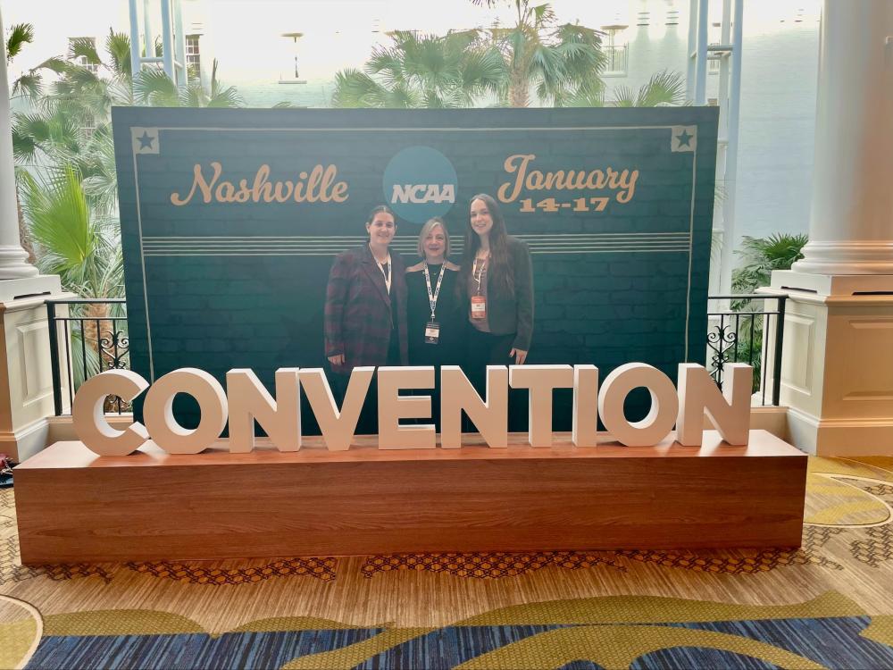 three women standing behind sign hat says Convention