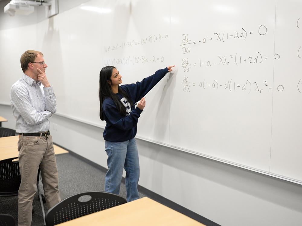 Two people in front of a white board