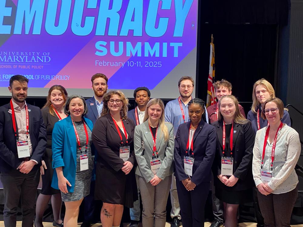 A group of students and faculty smiling in front of screen, during the at the Big Ten Democracy Summit.