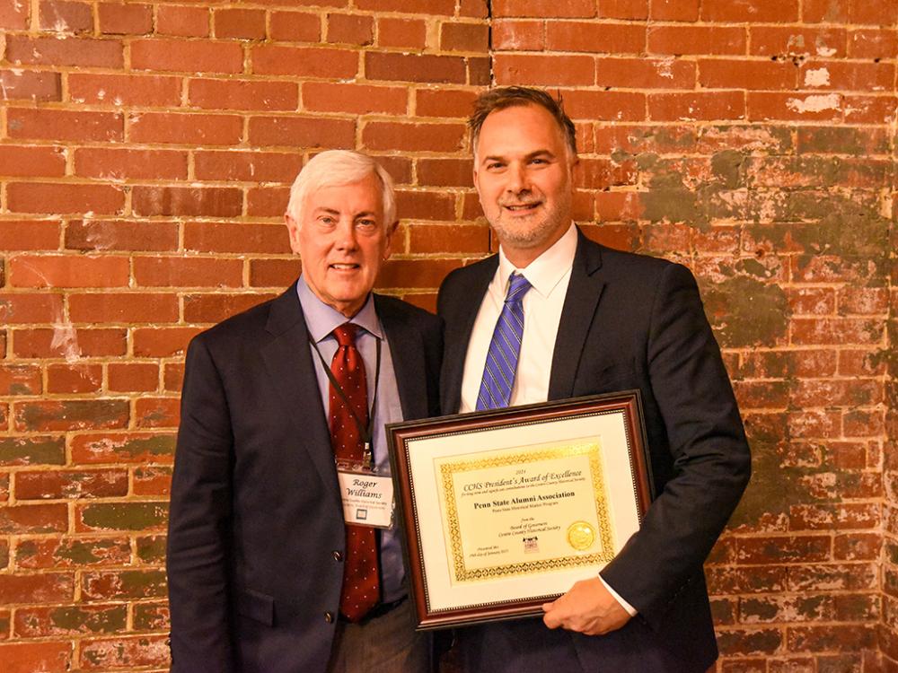 Two men stand together holding an award