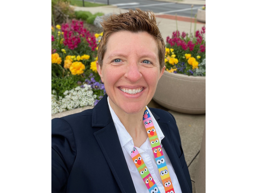 A person looks at the camera smiling standing in front of flowers.