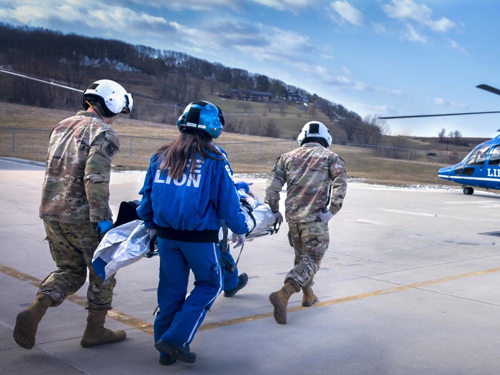 Three people carry a patient to a waiting helicopter