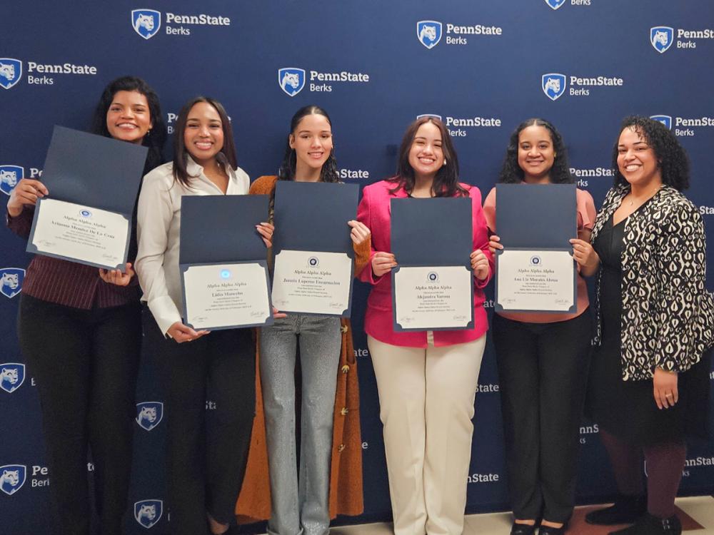 Five students hold certificates open with a staff member, all standing in front of a branded Penn State banner