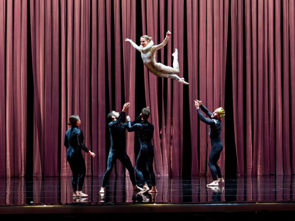 A group of acrobats circle to catch another in midair.