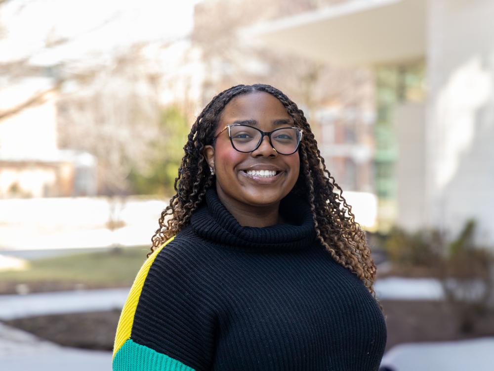 Noa Diggs poses outside academic buildings on a sunny day at Penn State University Park.