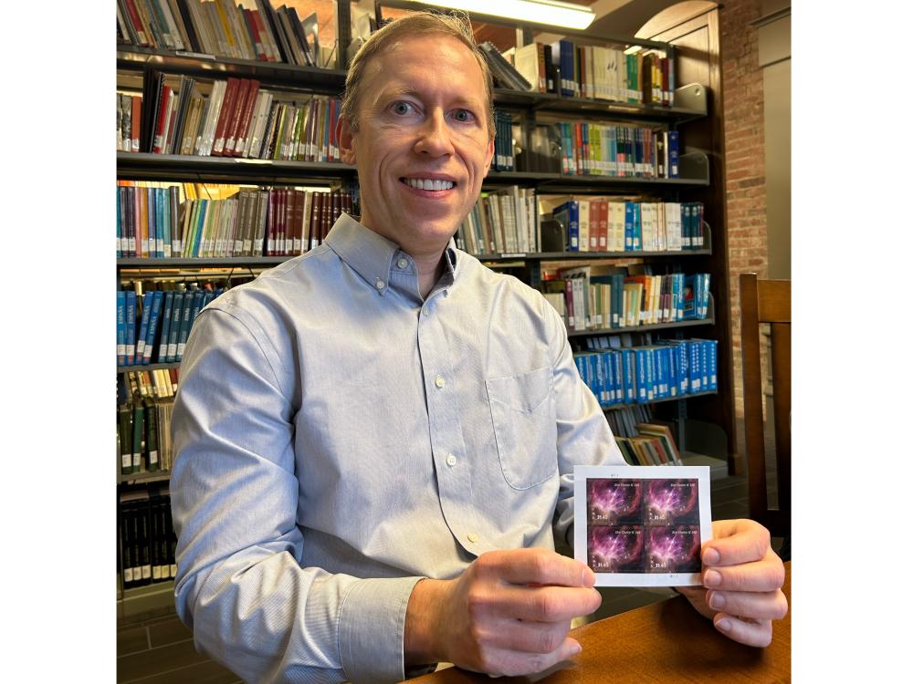 Image of Kevin Luhman holding a U.S. stamp with his image from the James Webb Space Telescope