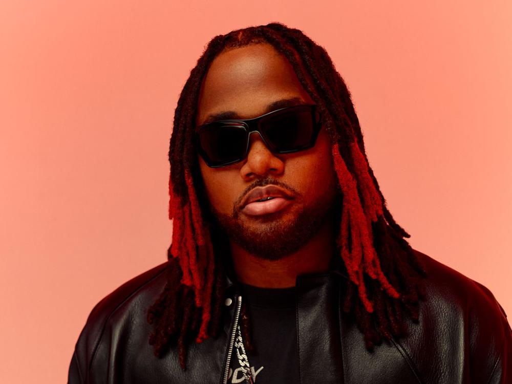 A Black man with dreadlocks wears sunglasses.