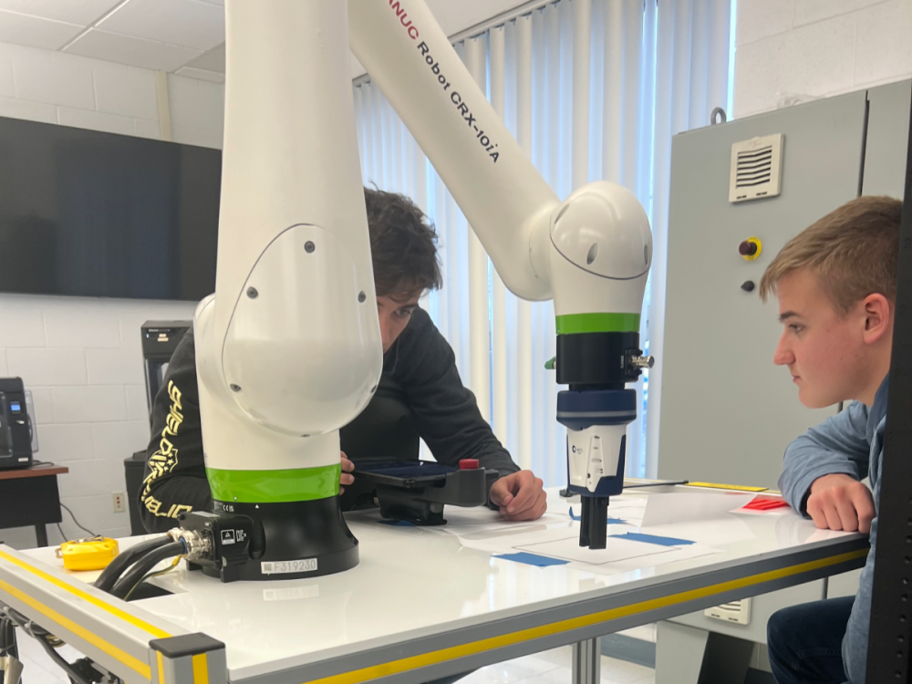 two students learning how to use a robot arm