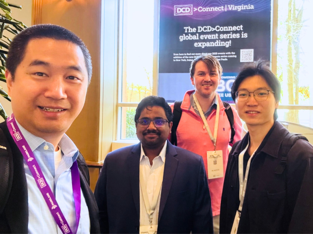 Four individuals stand in front of conference poster, all wearing conference lanyards