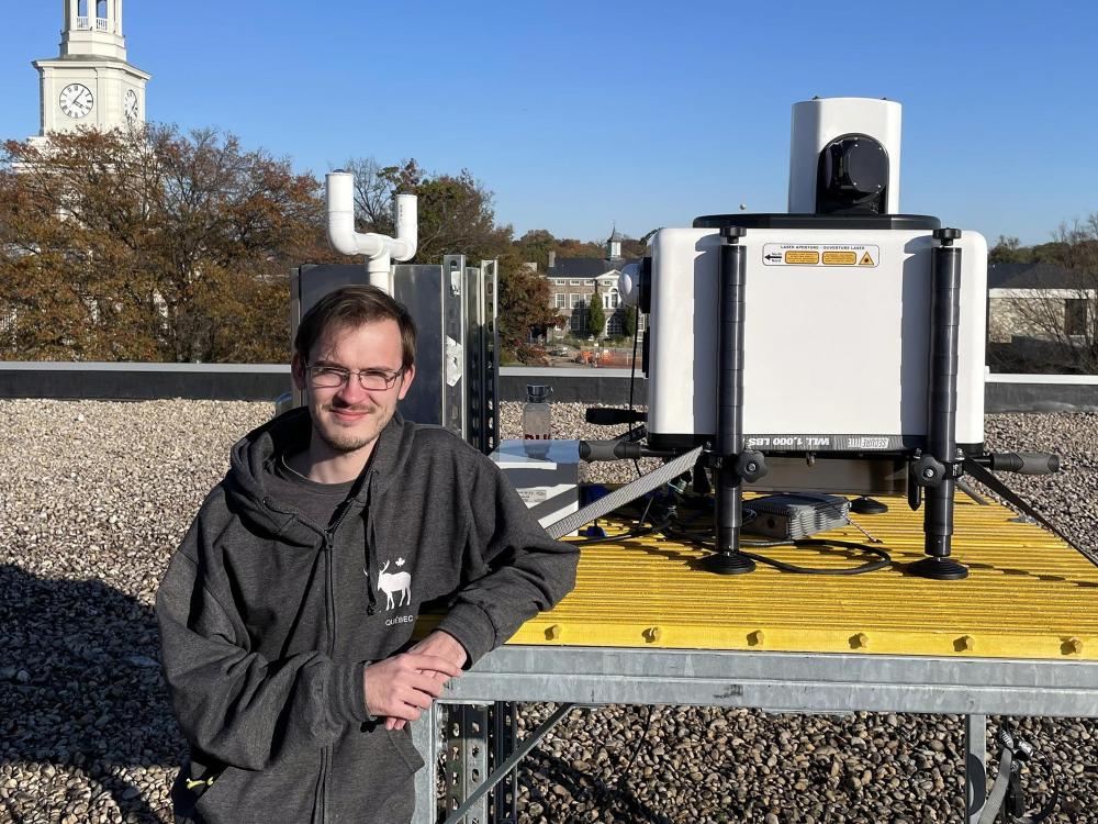 Graduate student Nicholas Prince stands next to LiDAR instrument