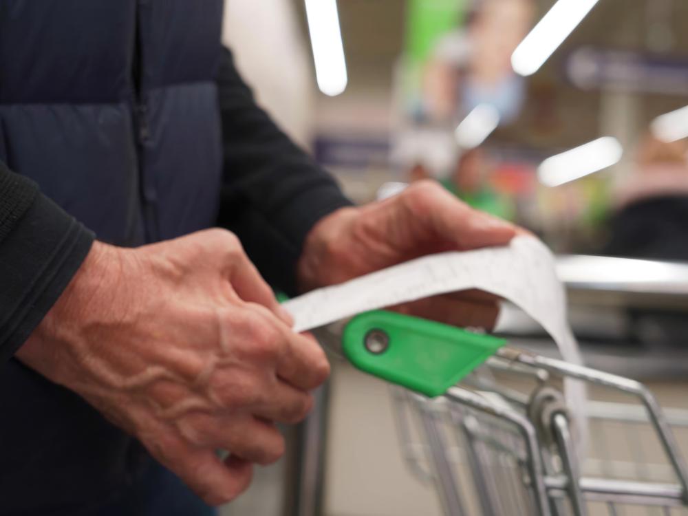 The hands of an older man holding a receipt over a shopping cart in a store