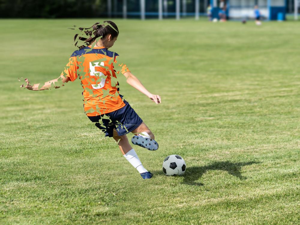 A girl wearing a soccer uniform goes to kick a soccer ball, but the girl has a digital effect that makes her look incomplete.