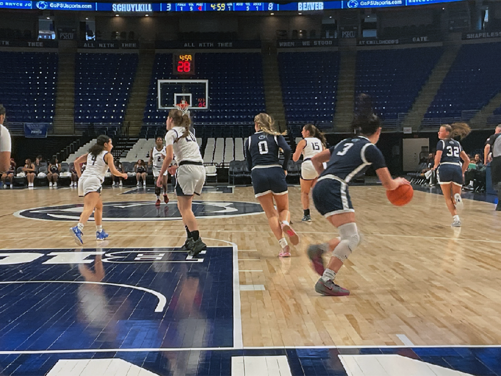 Women's basketball players wearing navy uniforms and white uniforms play on a court