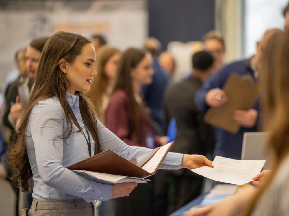 A female student hands a resume to a recruiter at Penn State Behrend's career fair.