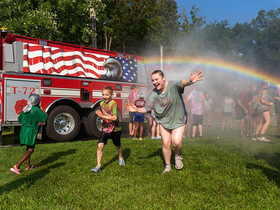 Students romp in the spray of water under a rainbow