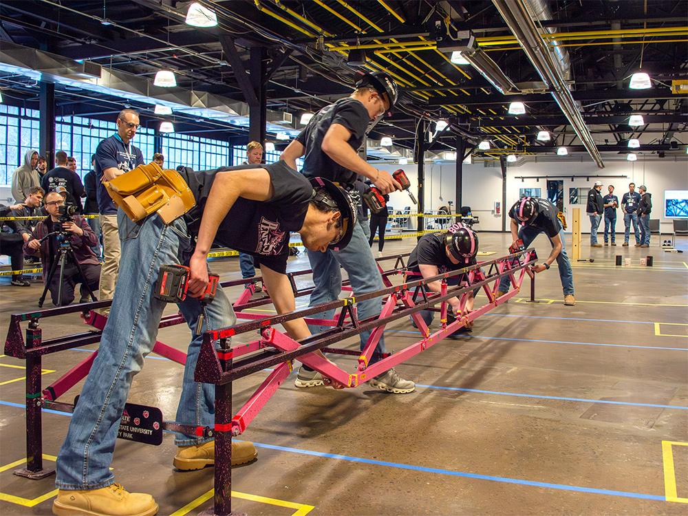 Students in a warehouse constructing a steel bridge to be used in a competition