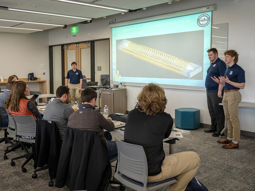 A group of people listen to a presentation given by students on the construction of their concrete canoe.