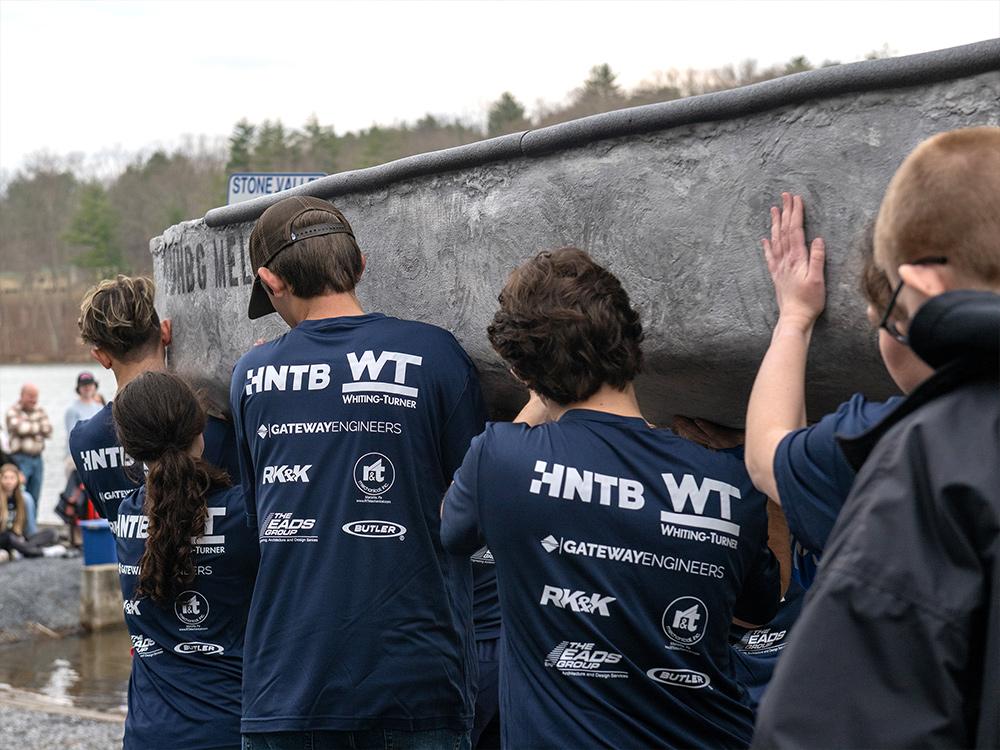 A team of students carry a concrete canoe out to the water