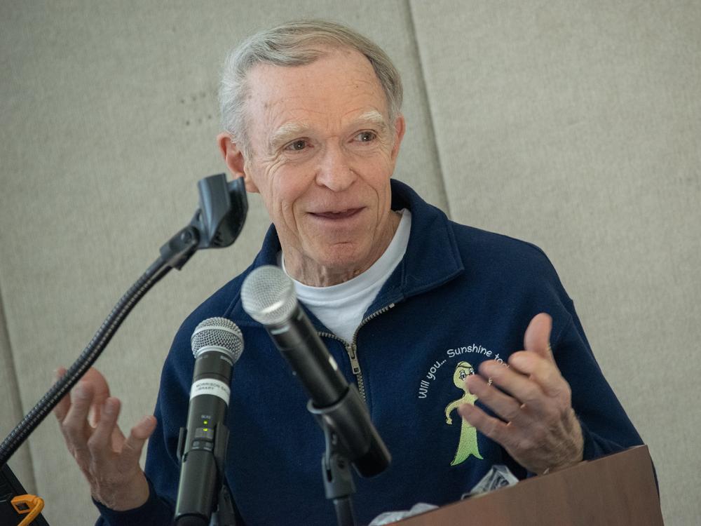 A man speaks at a podium from behind microphones
