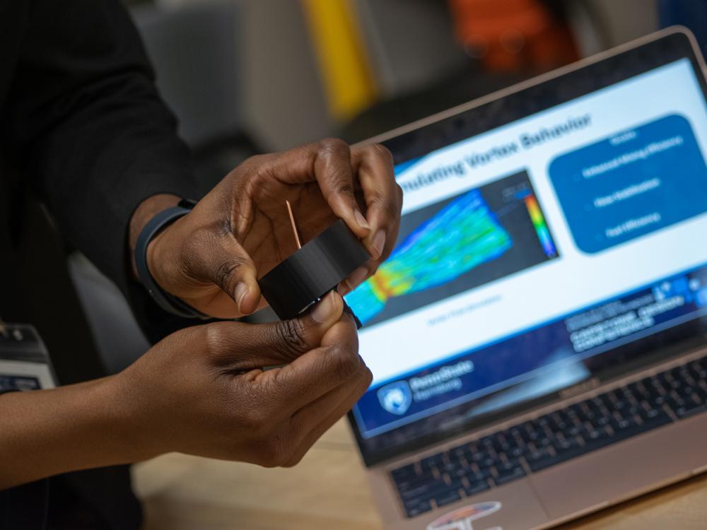Closeup of a person's hands holding pieces of a science project, with a laptop in the background