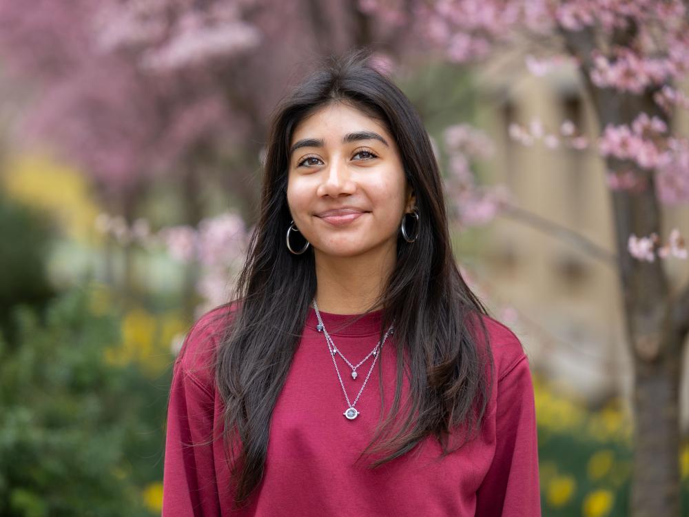 Jedily Alvarado stands in front of bushes and a flowering tree at Penn State University Park.