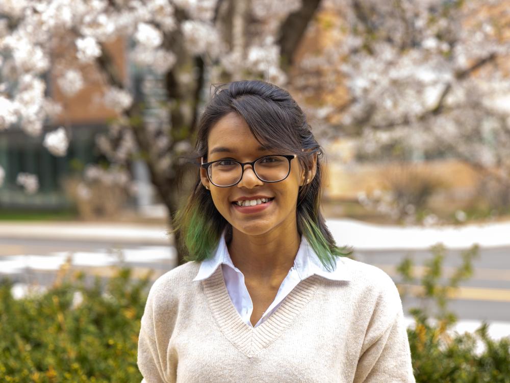 Halima Binte Islam stands in front of a flowering tree and bushes at Penn State University Park.