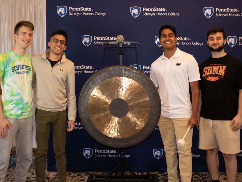 A group of 3 Schreyer Scholars pose with the gong