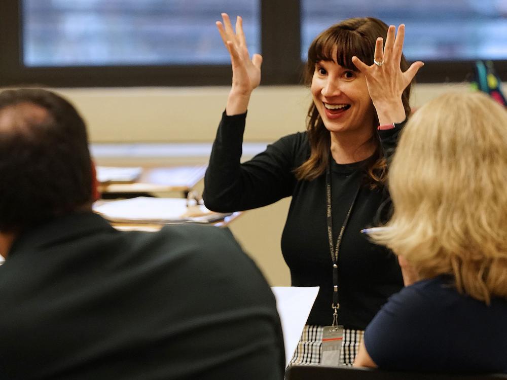 Teacher in dark shirt with her hands in the air during a discussion