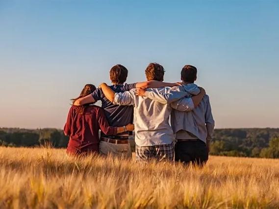 A group of youths standing in a field with the arms around one another