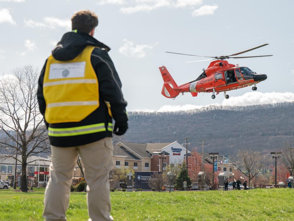 A person watches a red helicopter landing on a lawn