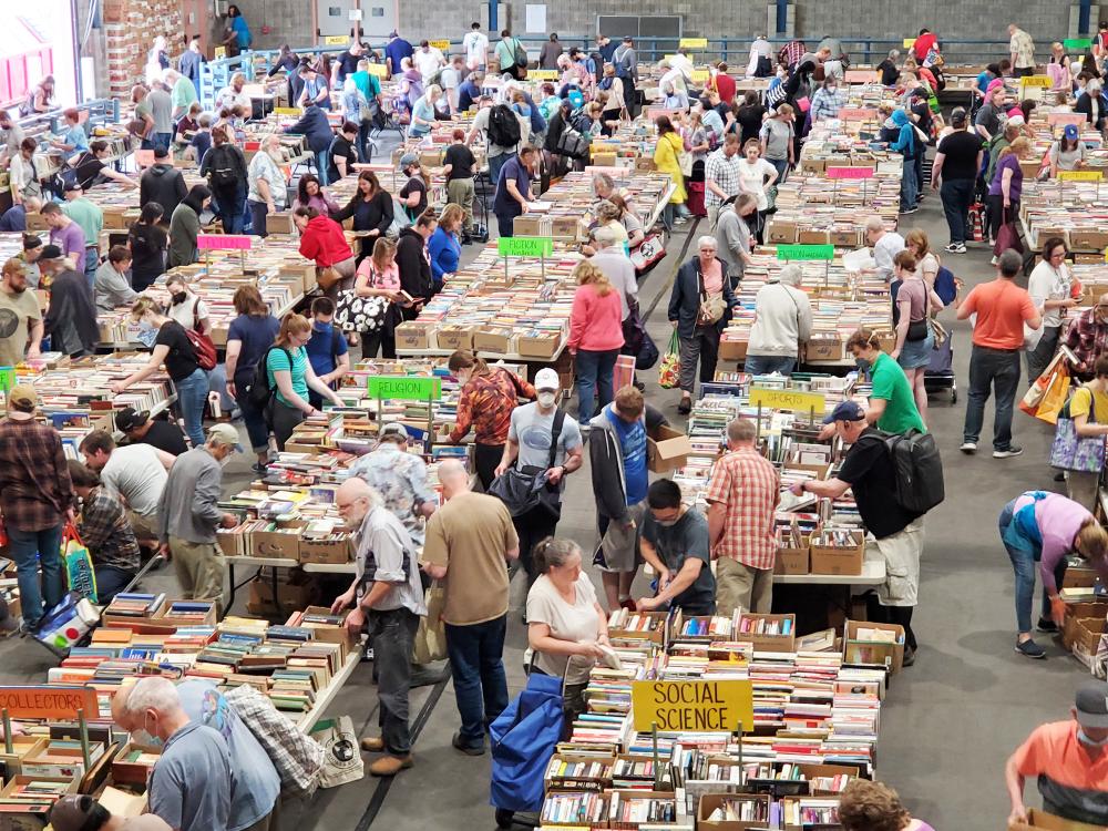 A large room full of shoppers browsing lots of books on tables
