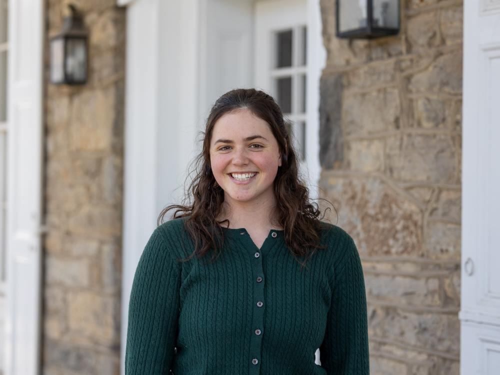 Lucy Taylor stands outside the University House wearing a green button-down sweater.