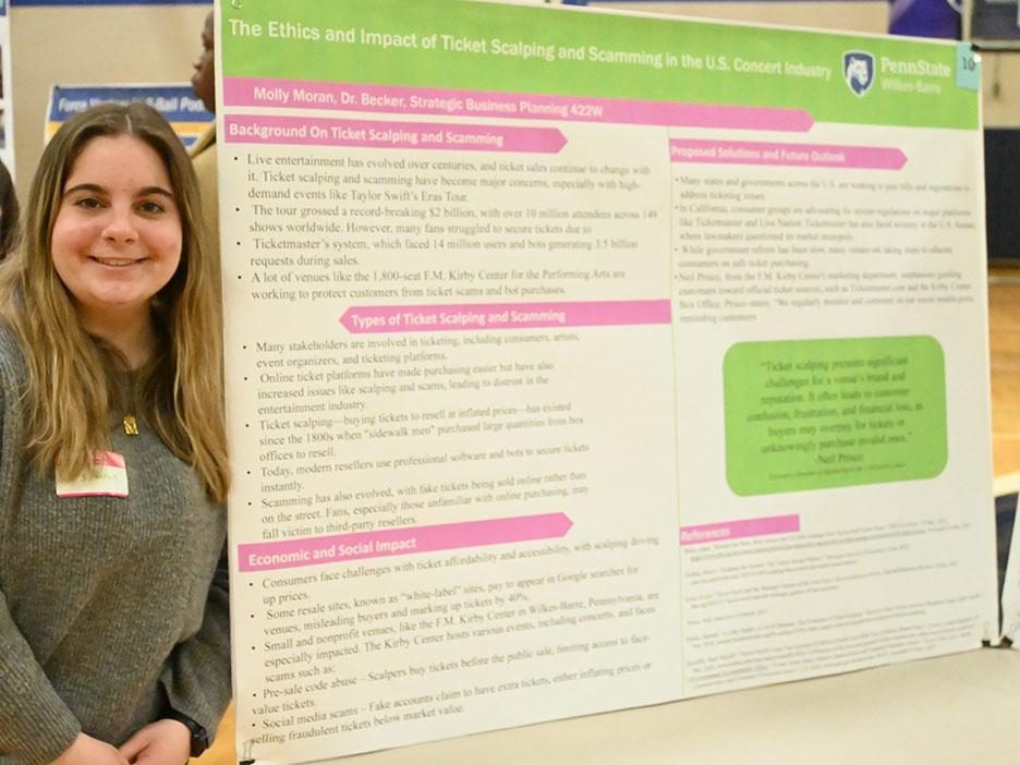 A woman stands at left next to a large research poster on a table.
