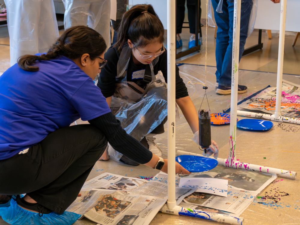 Two people crouch down to examine a science experiment on the floor
