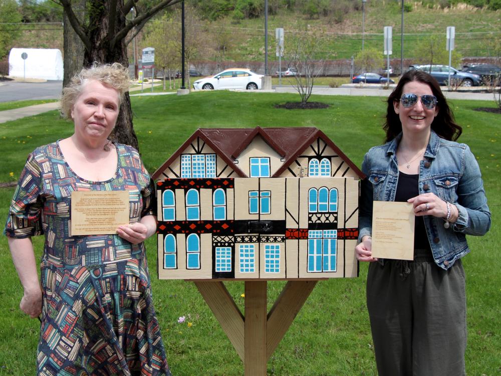 Jackie Atkins, assistant teaching professor of English, left, and Jessica Clontz, assistant teaching professor of human development and family studies, right, hold engraved plaques next to the Little Free Library that was installed and dedicated to the late Tony Vallone during a ceremony at Penn State DuBois on April 29.
