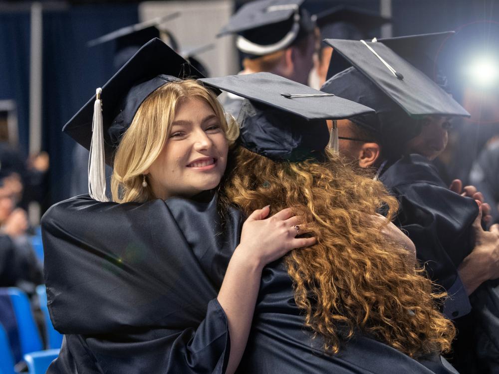 two students in graduation caps and gowns hug each other