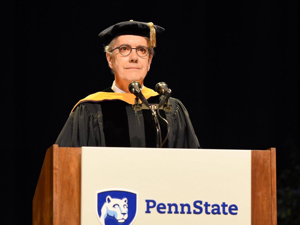 An individual wearing academic regalia stands at a podium.