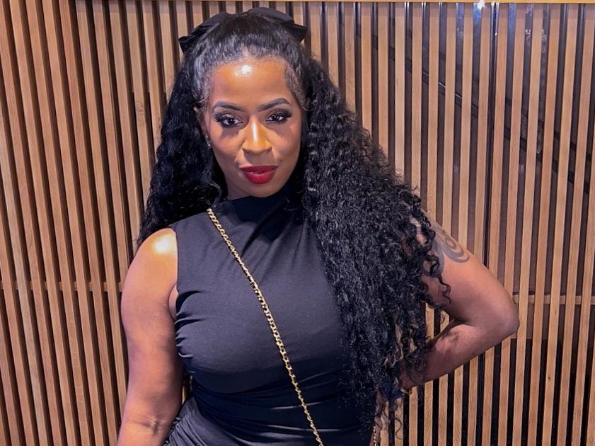 Felicia Ellis-Jones poses in a black dress in front of a wood slat wall.